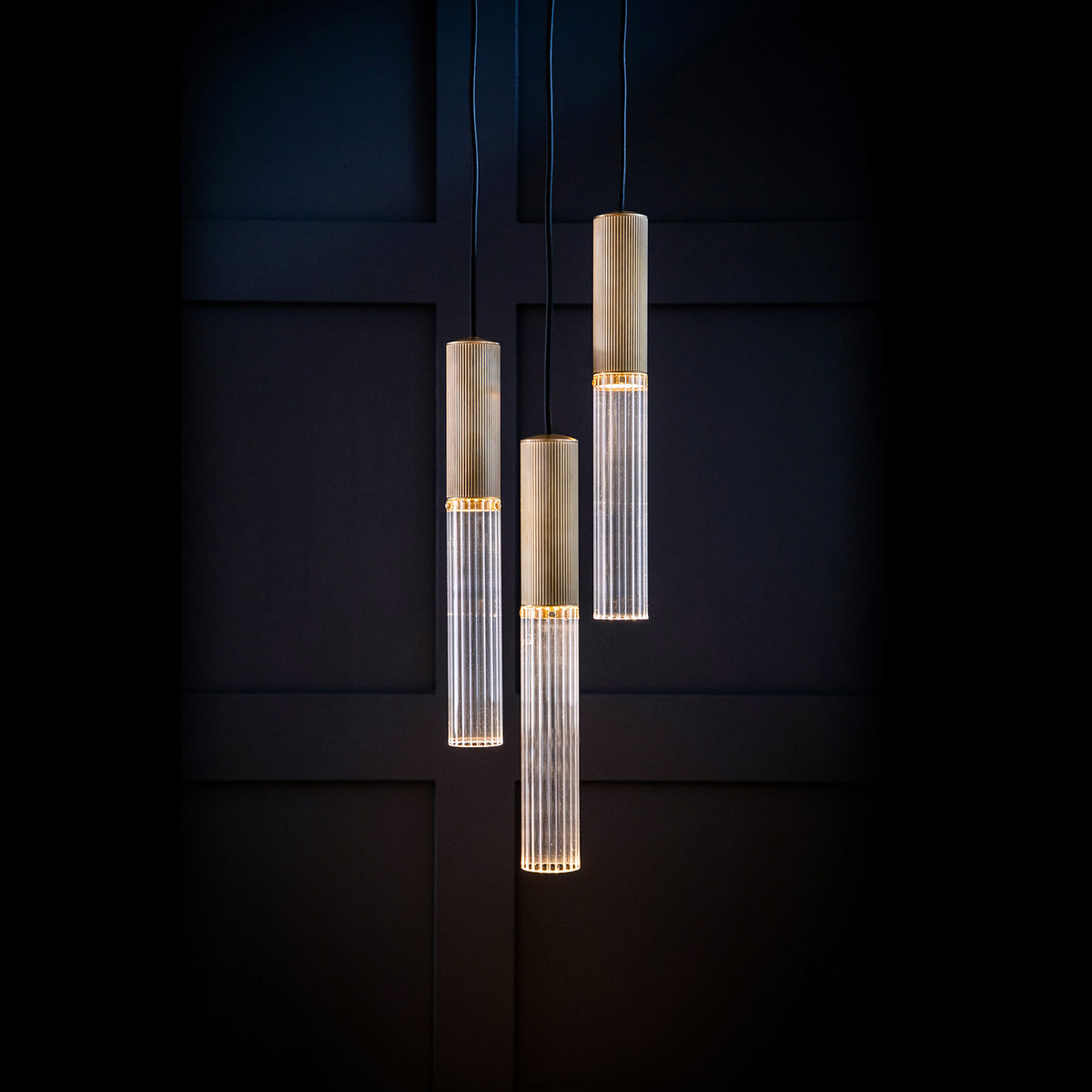 Brass and clear reeded glass Flume 50 triple pendant light in front of dark blue paneling
