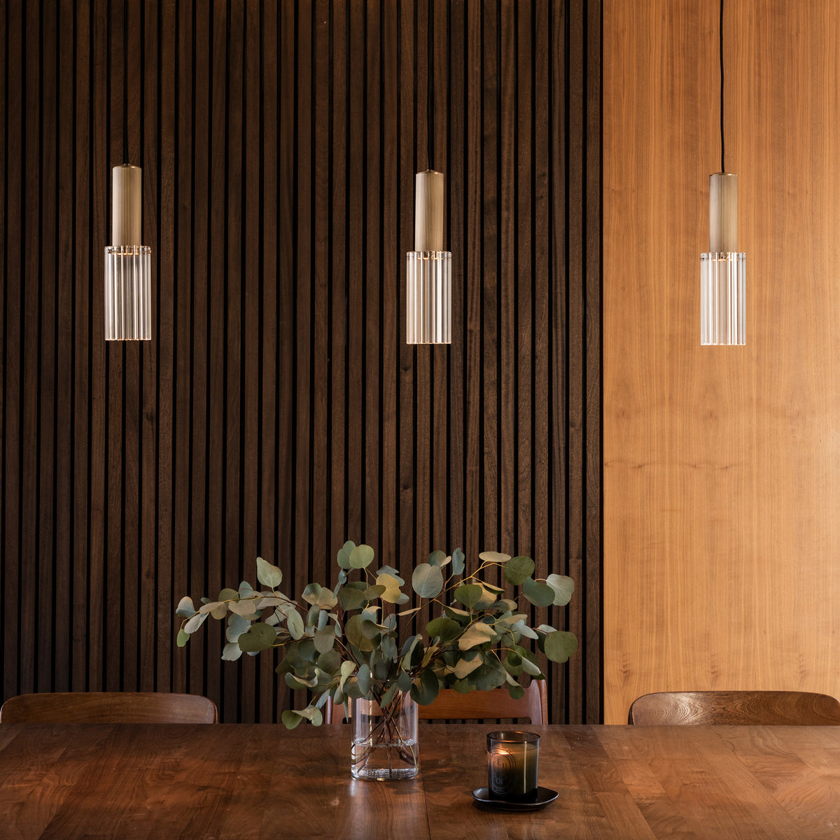 Three Flume 80 Pendant Lights in antique brass with clear reeded glass suspended above wooden dining table